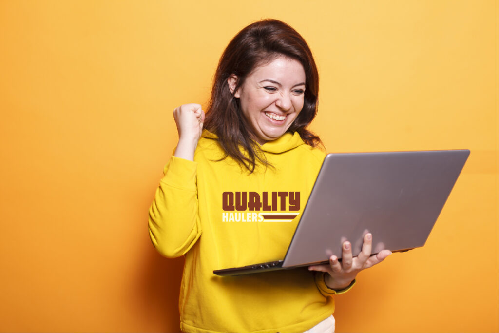 Get a Quality Free Quote!  Quality Haulers - Happy woman on computer in yellow hoodie on laptop.